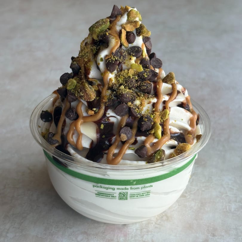 White soft-serve dessert topped with chocolate chips, pistachios, and chocolate and caramel drizzles.