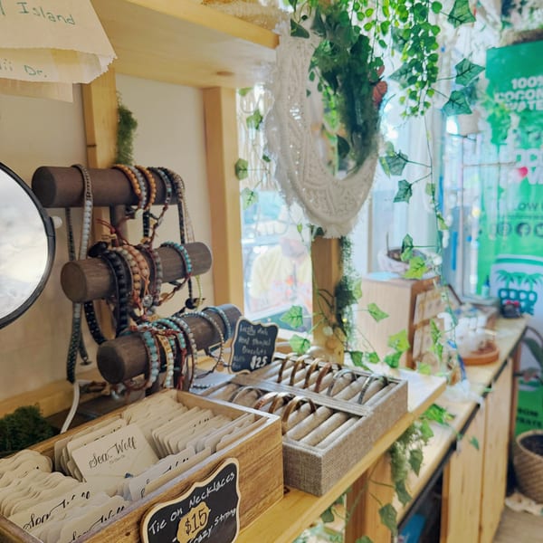 A cafe display of bracelets and necklaces on wooden stands, with green vines and natural light.