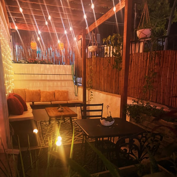 Cozy outdoor patio at night with string lights, bamboo walls, and cushioned seating.