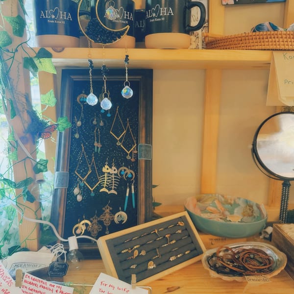 A display of Journey Cafe Big Island merchandise, including mugs, earrings, rings, and bracelets.