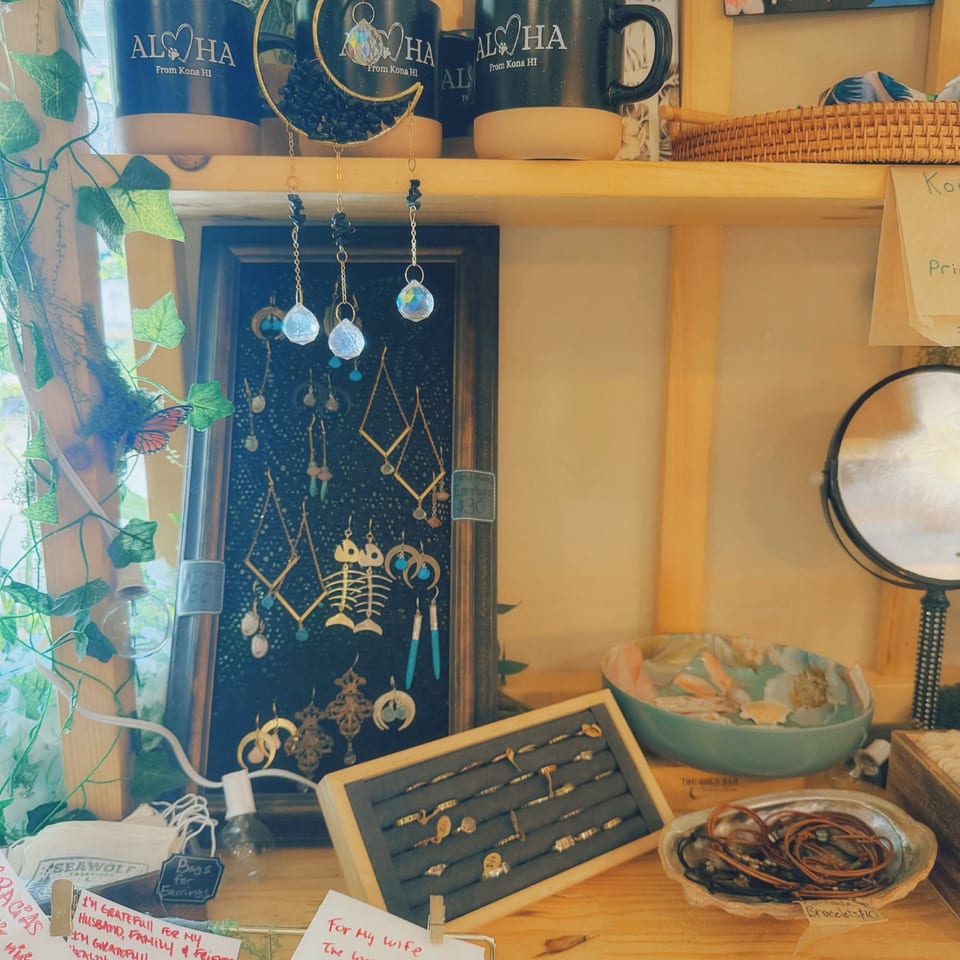A display of Journey Cafe Big Island merchandise, including mugs, earrings, rings, and bracelets.