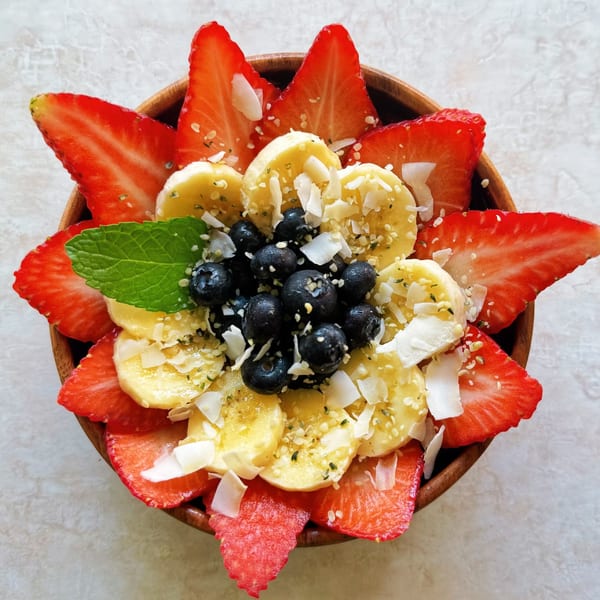 A vibrant fruit bowl with strawberries, bananas, blueberries, mint, and coconut flakes.