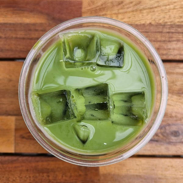 Overhead view of an iced green matcha latte with ice cubes in a clear cup on a wooden table.