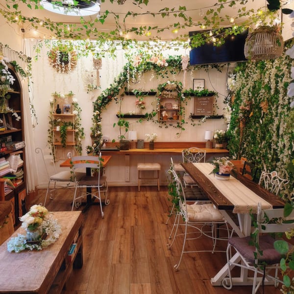 Journey Cafe interior with ivy, string lights, white chairs, and wooden tables creating a cozy atmosphere.