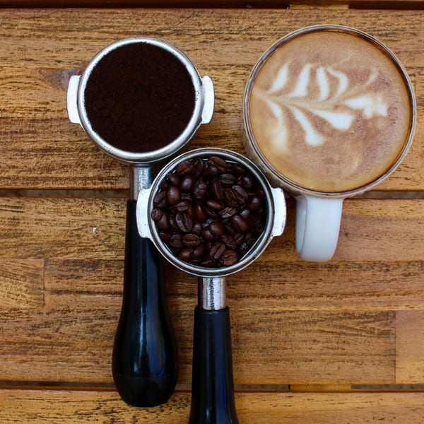 Overhead view of coffee beans, ground coffee, and a latte with art on a wooden table.